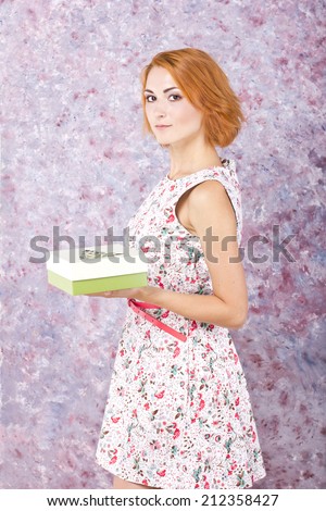 Charming young girl holding a gift box. Bright oil background. Hair style. Red short hair