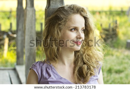 Beautiful smiling girl sitting on the porch of a wooden house.Beautiful curly blonde outdoors. Portrait of a happy woman.