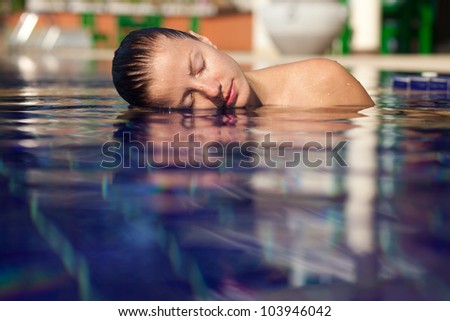 Beautiful young woman in the pool. Left half of her face and shoulder above the water