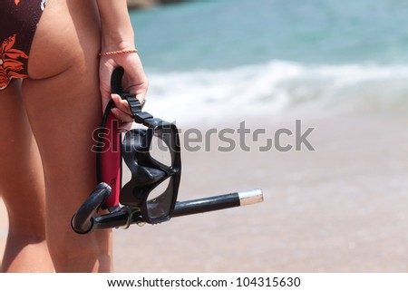 Young woman in swimsuit is on the beach and holding a mask and snorkel diving