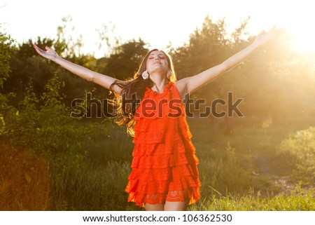 Pretty woman in a bright red dress stretching out her hands, enjoying the sun and aroma of nature