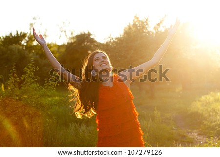 Happy woman in a bright red dress stretching out her hands, enjoying the sun and aroma of nature
