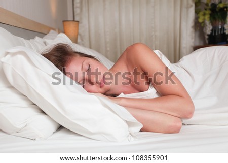 A young attractive woman lying on a bed with white sheets