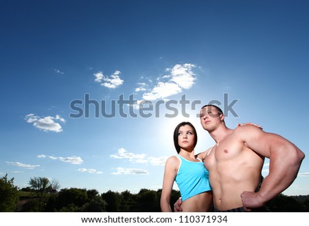 Beautiful athletic man and woman standing in embrace against the blue sky