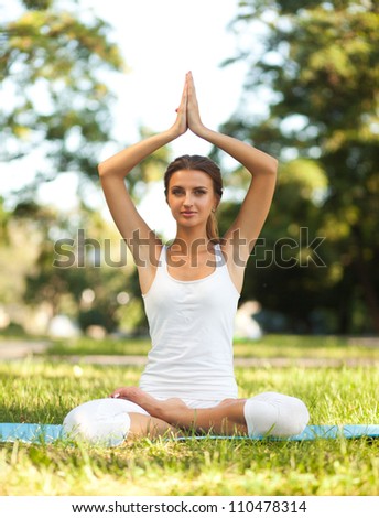 Beautiful young woman practices yoga in nature. Lotus pose, hands over her head