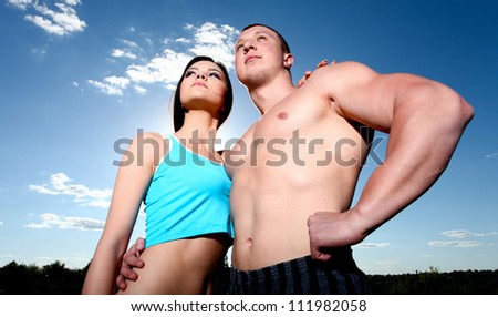 Beautiful young athletic man and woman standing in embrace against the blue sky