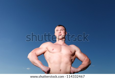A handsome young athletic and muscular man standing against the blue sky