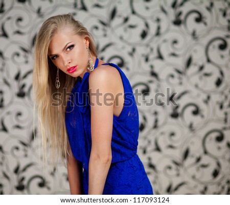 Portrait of stunning young woman in blue dress against the gray vintage wallpaper