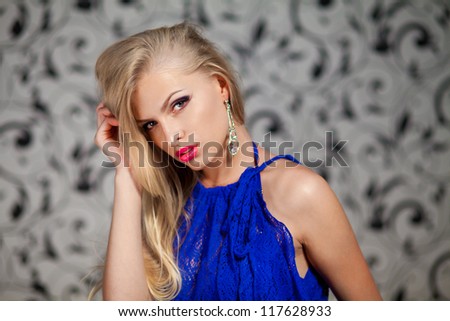 Portrait of young woman in blue dress against the gray vintage wallpaper