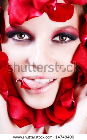 The face of beautiful young girl is surrounded by petals of red rose