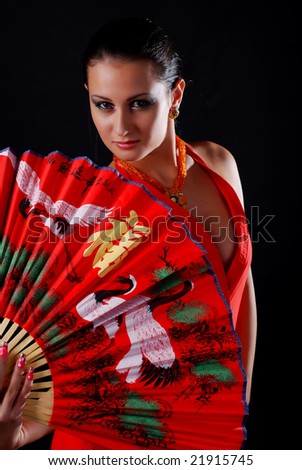 beautiful brunet woman in red clothes with fan at black background