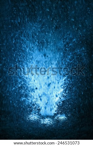 Colorful fountain splashes light blue and white color of water drops on a black background. motion blur