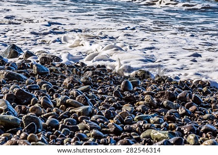 Stones and water with foam and waves on the beach coast or shore of ocean or sea