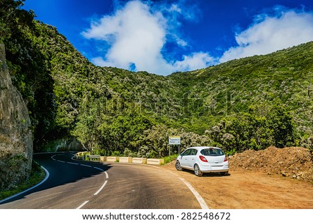Asphalt road and white car or auto in green mountains or rocks with blue sky and clouds in Tenerife Canary island, Spain at spring or summer