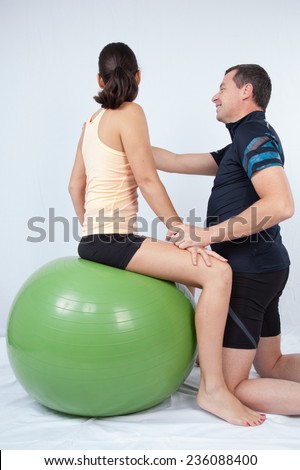 Man at the gym doing excercices to a woman with a swiss ball