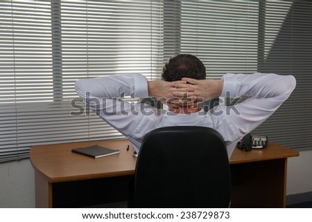 A relaxed business man keeping hands behind head