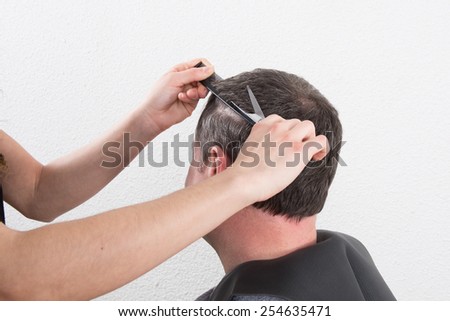 Hairdresser trimming man\'s brown hair with scissors