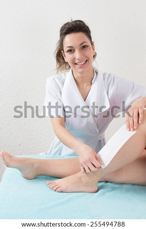 Beautician waxing a woman\'s leg applying wax strip