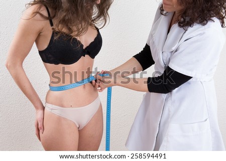 Slim woman measuring waist with tape measure in centimeters