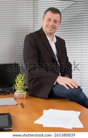 Business man sitting on desk in his office looking at camera