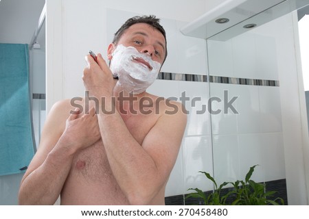 Man shaving with a razor blade and shaving cream in bathroom