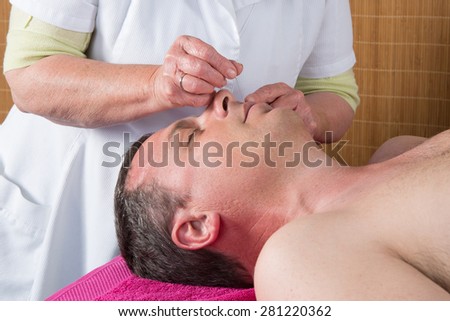 Acupuncturist prepares to tap needle around face  of man