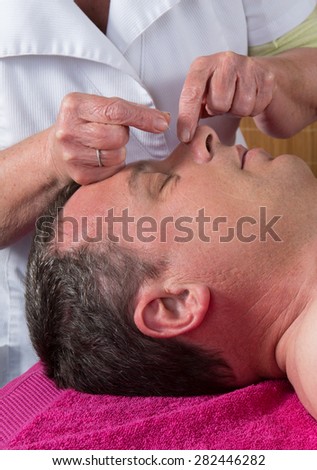 Acupuncturist prepares to tap needle around face  of man