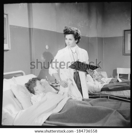 LJUBLJANA, YUGOSLAVIA (SLOVENIA) - circa 1950: Vintage photo of children's hospital room with a young female doctor attending her patients, checking boy's pulse.