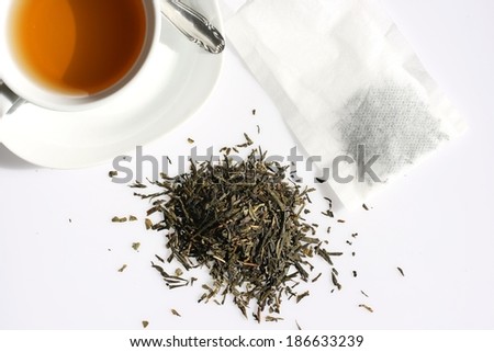 Organic green tea dried leaves with cup of tea and filter bag, pictured from above