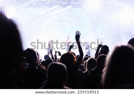 People attending pop concert, silhouettes of crowd dancing in front of stage, shallow DOF