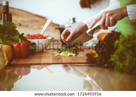 Unknown human hands cooking in kitchen. Woman slicing green onion. Healthy meal, and vegetarian food concept