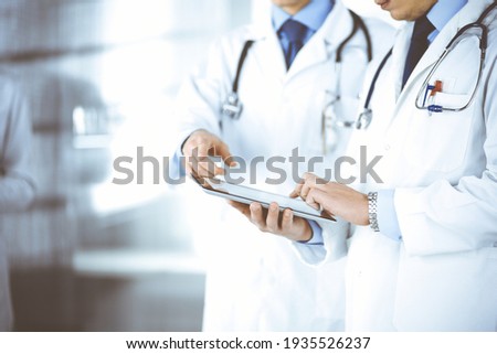 Group of unknown doctors use a computer tablet to check up some medical names records, while standing in a hospital office. Physicians ready to examine and help patients. Medical help, insurance in Stock fotó © 