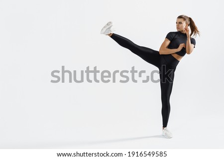 Confident female athlete workout, practice leg kicks, kicking air in sportswear. Muscular trained woman kicking with raised feet, exercise kickboxing moves, white background.