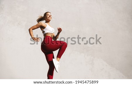 Fit woman exercising outdoors. Healthy young female athlete doing fitness workout. Sportswoman raising leg, do functional training outside on bright sunny day, smiling pleased, wearing sport outfit