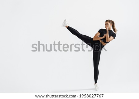 Determined sport woman in activewear do high kick, tae-bo martial arts exercises isolated on white background. Athletic fit girl with perfect body kick air, punching with legs, practice kicks