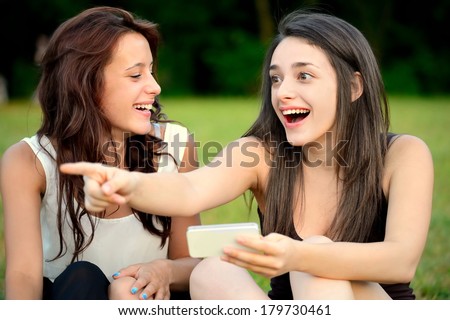 Two beautiful young women in a park one of them points at something with amazed face