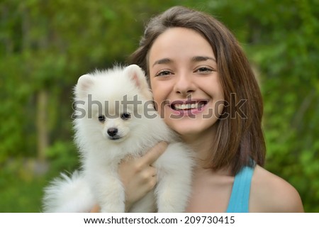 Attractive young woman holding german spitz puppy outside and smiling at camera.