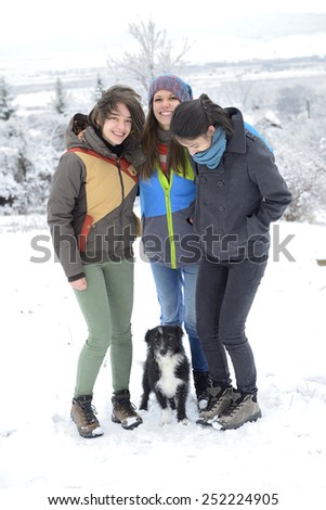 Three young women having having fun with small black dog outside in winter.
