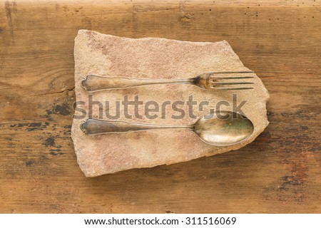 antique spoon and fork on sandstone slab on wooden background