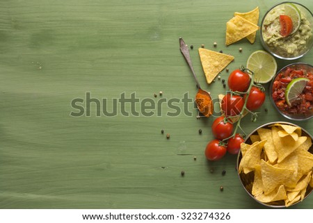 Tortilla chips arranged on wooden surface with guacamole and salsa