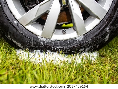 Clean car wheel rim after washing with car shampoo, foam on the grass. Car wash in nature and summer cottage Stock fotó © 