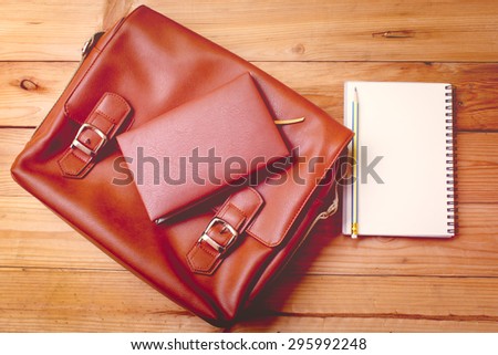 leather female bag with note book on wood background.