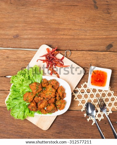 Thai fried fish cake (Tod Mun Pla) or prawn fritter ball with dipping red sauce and spoon Thai food traditional recipe on wooden background