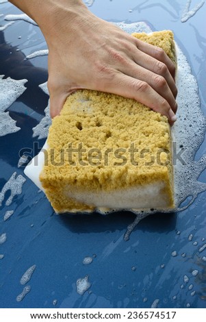male hand is cleaning  car bonnet with yellow sponge; selective focus at hand