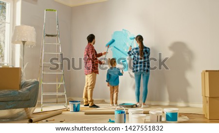Family Time Together with Small Daughter. Young Father and Mother Showing Their Child How to Paint a Wall with a Roller. Paint Color is Light Blue. Room at Home is Prepared for Renovations. Foto stock © 