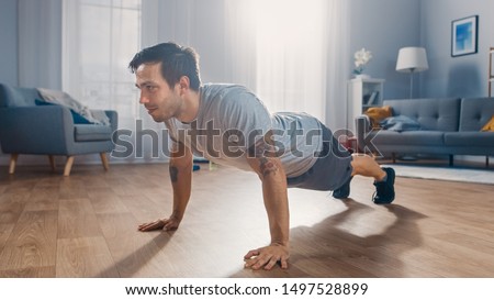 Muscular Athletic Fit Man in T-shirt and Shorts is Doing Push Up Exercises at Home in His Spacious and Bright Apartment with Minimalistic Interior. Foto stock © 