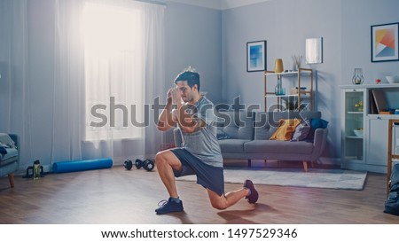 Strong Athletic Fit Man in T-shirt and Shorts is Doing Forward Lunge Exercises at Home in His Spacious and Bright Apartment with Minimalistic Interior. Сток-фото © 
