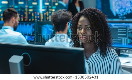 Female Computer Engineer Works on a Neural Network/ Artificial Intelligence Project with Her Multi-Ethnic Team of Specialist. Office Has Multiple Screens Showing 3D Visualization.