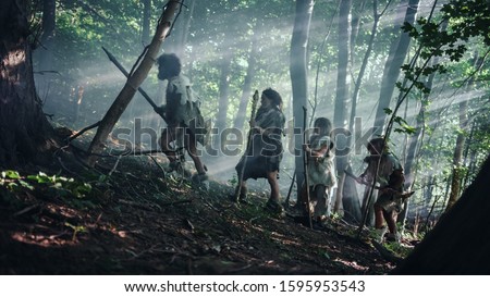 Tribe of Hunter-Gatherers Wearing Animal Skin Holding Stone Tipped Tools, Explore Prehistoric Forest in a Hunt for Animal Prey. Neanderthal Family Hunting in the Jungle or Migrating for Better Land