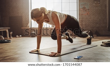 Beautiful and Young Girl Doing Running Plank on Her Fitness Mat. Athletic Woman Does Mountain Climber Workout in Stylish Hardcore Gym ストックフォト © 
